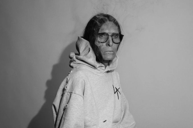Monochrome portrait of an older person wearing eyeglasses and a distressed light grey hoodie with smoke swirling above