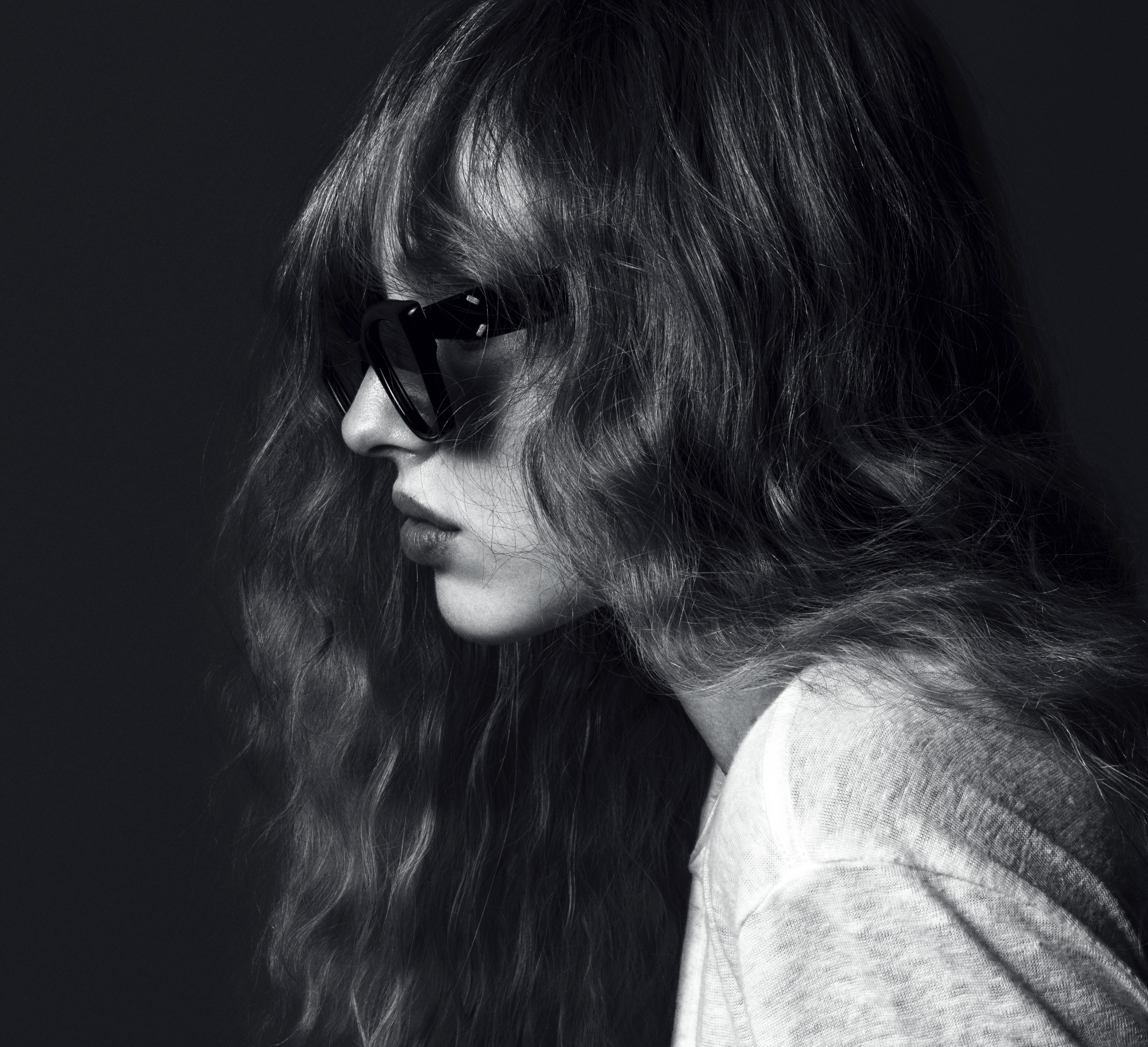 Monochrome close-up of an adult woman with sunglasses and wavy long hair, captured in a studio setting with a neutral background.