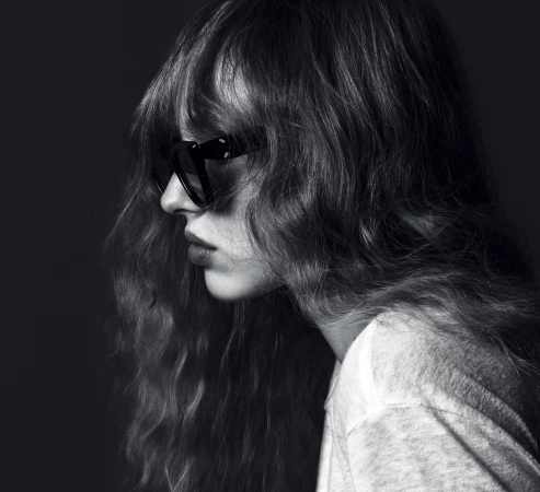 Black and white profile portrait of a woman with long wavy hair and dark sunglasses wearing a white top