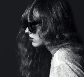 Black and white profile portrait of a woman with long wavy hair and dark sunglasses wearing a white top