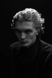 Portrait of a man with wavy hair wearing a dark shirt against a black background