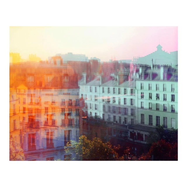 Cityscape view with multiple buildings in Paris, France, featuring residential buildings, rooftops, and trees against a soft, colorful sky.