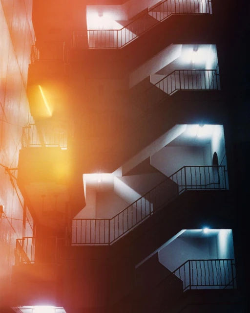 Architectural nighttime exterior of a modern building featuring an emergency staircase with iron railings and electric lighting.