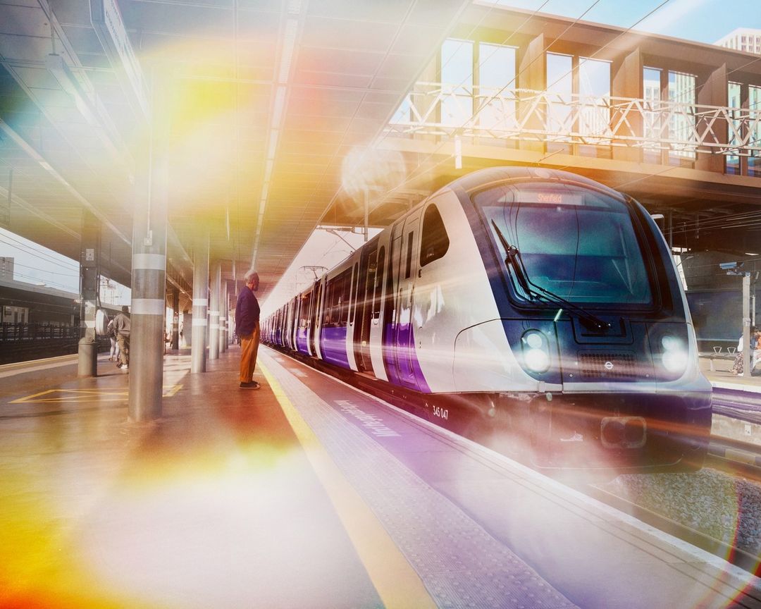 Train arriving at a station with a man waiting on the platform, featuring modern architecture and bright, natural lighting.