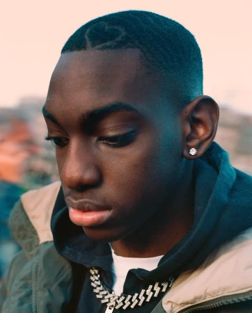 Close-up portrait of a young Black man with a shaved heart design in his hair, wearing a silver chain and hoodie, by Ben Stockley.