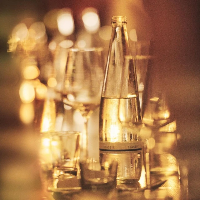 Elegant still life of clear glass water bottle and assorted glassware filled with liquid, set against a blurry, golden-toned background.