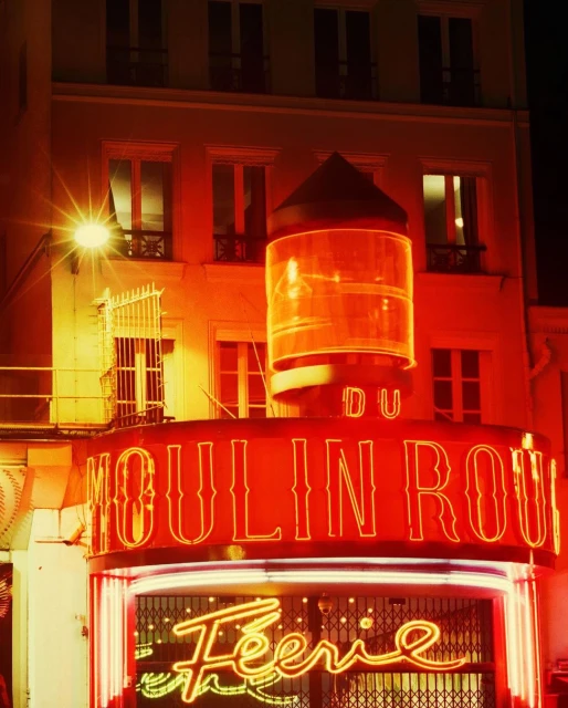 Illuminated Moulin Rouge cabaret sign in Paris, France at night. Iconic architecture and neon lighting create a vibrant scene.