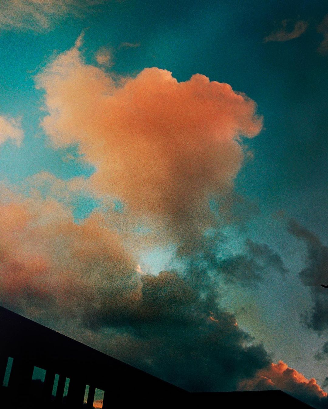 Dramatic sky with pink and blue clouds against a dark building silhouette at the bottom of the frame during the day.