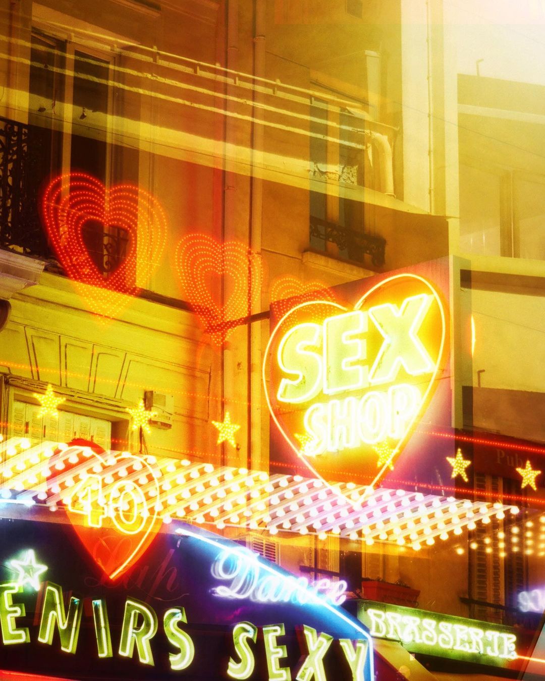 Illuminated storefront with neon signs for 'Sex Shop,' hearts, and erotic dance in an urban setting at night, creating a vibrant atmosphere.