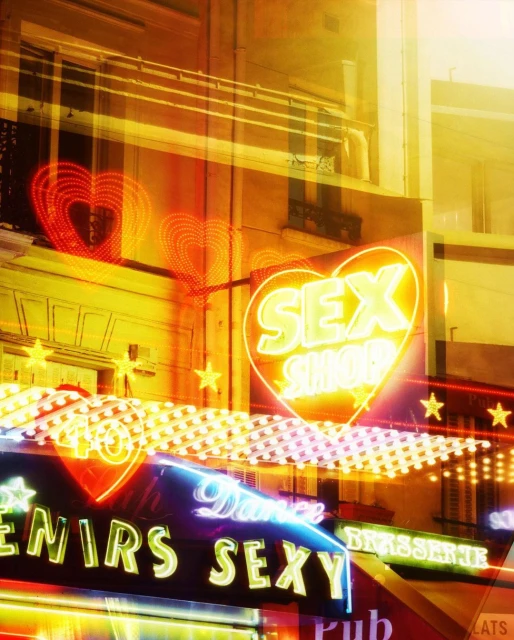 Brightly lit neon signs adorn a building at night, featuring heart shapes, stars, and text like 'Sex Shop' and 'Dance Sexy.'