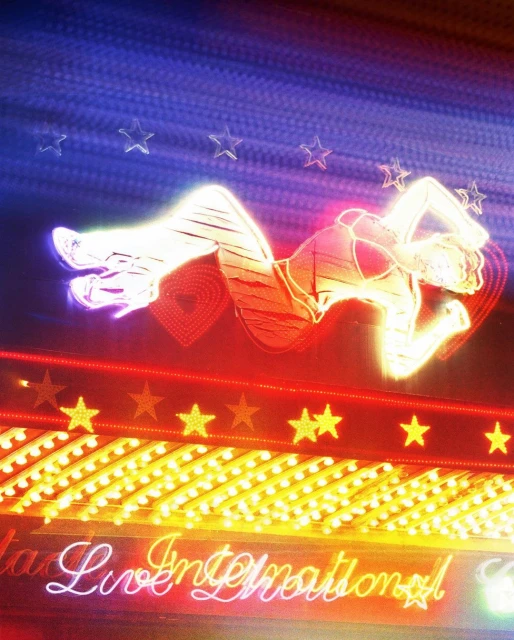 Neon sign featuring a woman in a reclining pose surrounded by stars, hearts, and illuminated cursive text on a blue and red background.