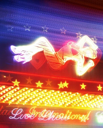 Neon sign featuring a woman in a reclining pose surrounded by stars, hearts, and illuminated cursive text on a blue and red background.