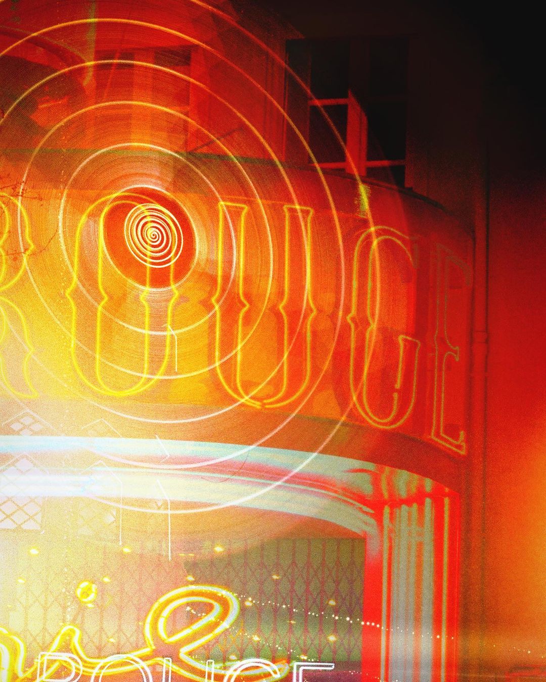 Abstract nighttime cityscape with neon signage of a building featuring red, orange and white lights and geometric spiral design elements.