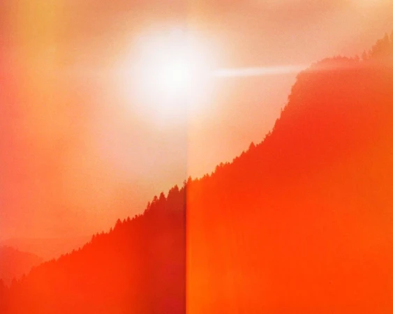 Orange-toned mountain range with silhouetted trees ascending the slopes under a bright light source.