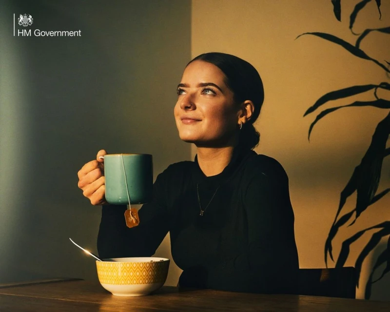 A young woman sits at a table with a cup of tea and a bowl, bathed in soft light, creating a serene and peaceful atmosphere.