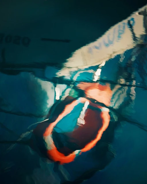 Abstract view of orange lifeguard float in pool water, showing a blurred reflection with white and dark-blue tones; swimming pool safety equipment.