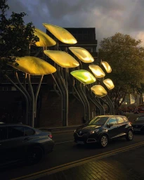 Illuminated leaf-shaped art installation lining a city street at dusk with cars driving past