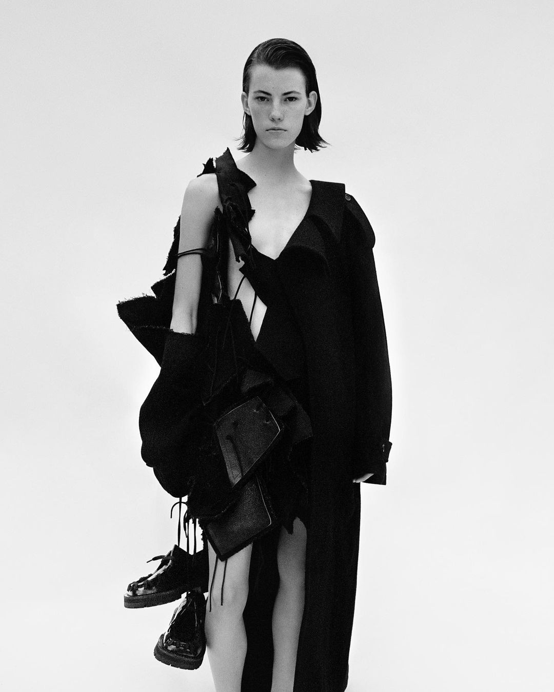 Model with slicked back hair wearing a black avant garde coat against a solid white background