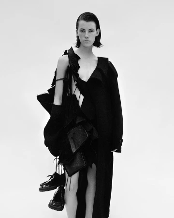 Model with slicked back hair wearing a black avant garde coat against a solid white background