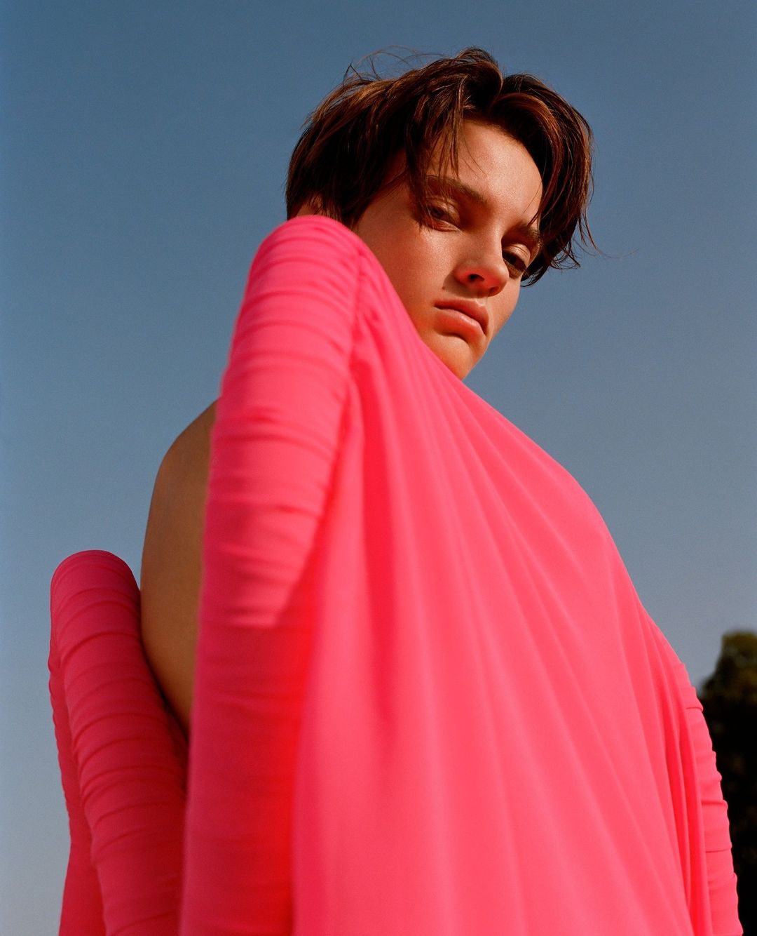 Model in vibrant pink top photographed from a low angle against a clear blue sky by Ben Toms