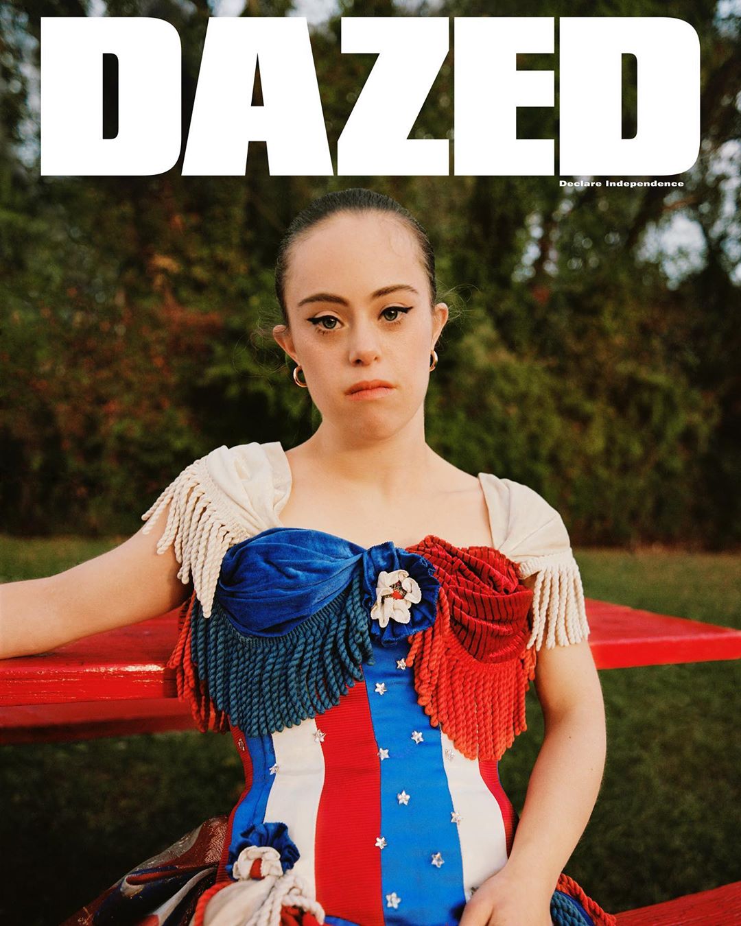 Portrait of a person with Down syndrome wearing a patriotic dress in a field, magazine cover for 'Dazed' with text overlay.