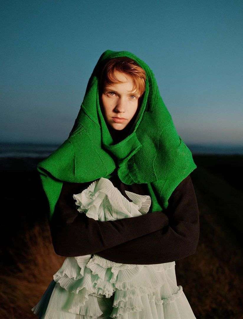 Fashionable woman with green textured shawl and ruffled dress, outdoors, with a serene expression.