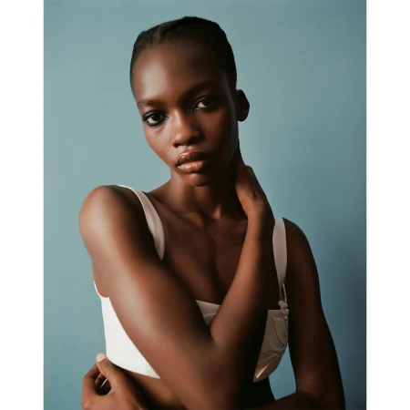 Portrait of a black woman wearing a white top with one hand on her neck against a muted blue background by Ben Toms
