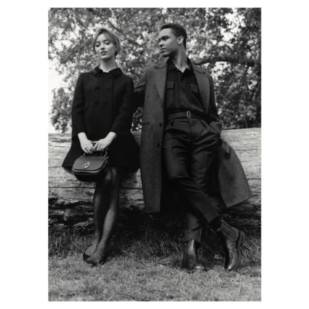Black and white fashion shot of an adult couple posing outdoors, leaning against a fallen tree in a park setting, wearing dress clothes.