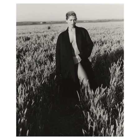 Black and white portrait of a woman in a coat standing in a wheat field, monochromatic and textural, with a rural outdoor setting.