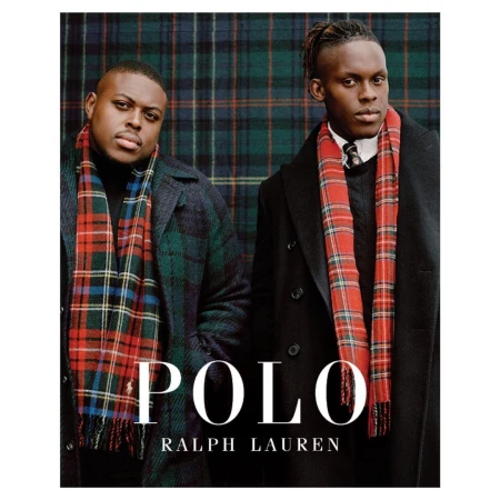 Two adult males stand indoors against a tartan backdrop, wearing dark overcoats and scarves in a fashion editorial by Polo Ralph Lauren.