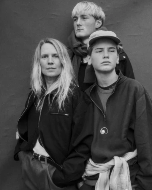 Black and white portrait of a family of three, featuring a woman with long blonde hair, a teenage boy in a baseball cap, and an adult man.