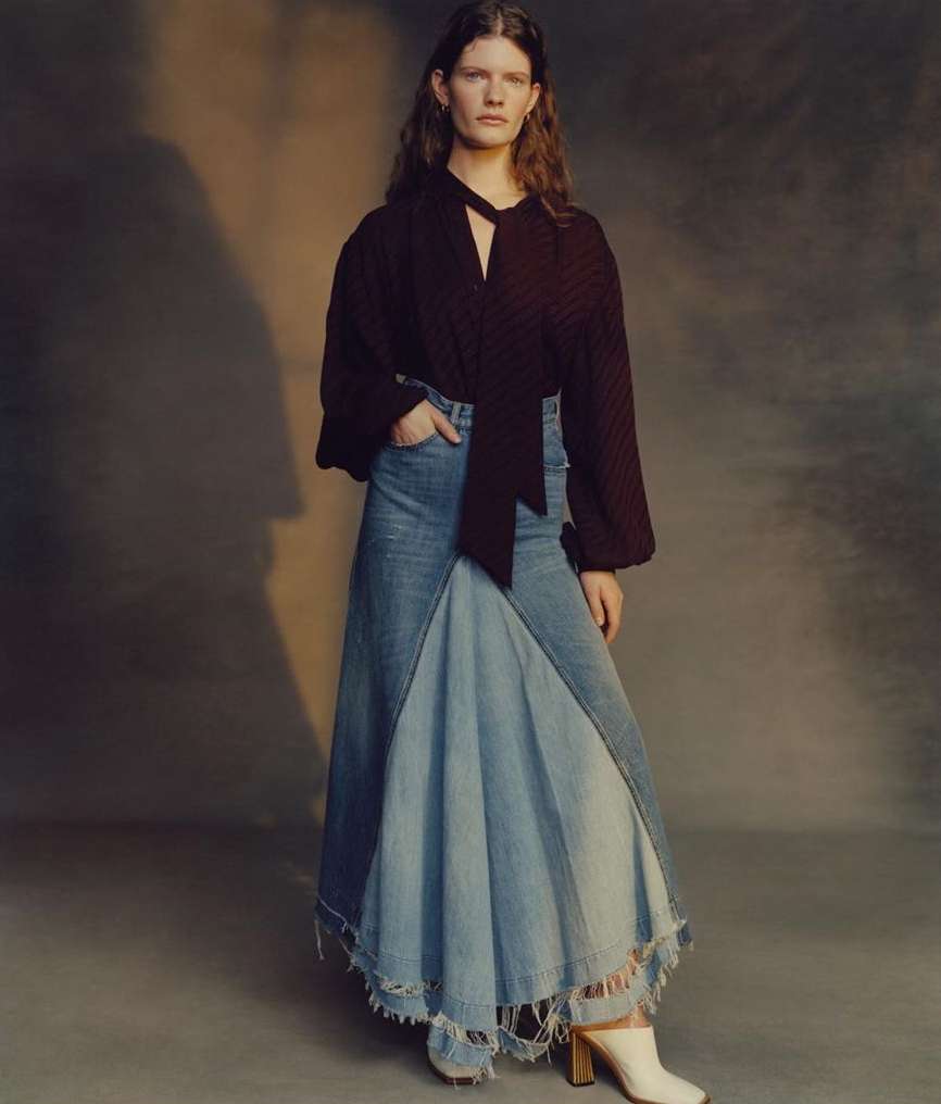 Woman in a dark top and denim patchwork skirt poses in a studio setting, creating a fashionable and visually striking image.