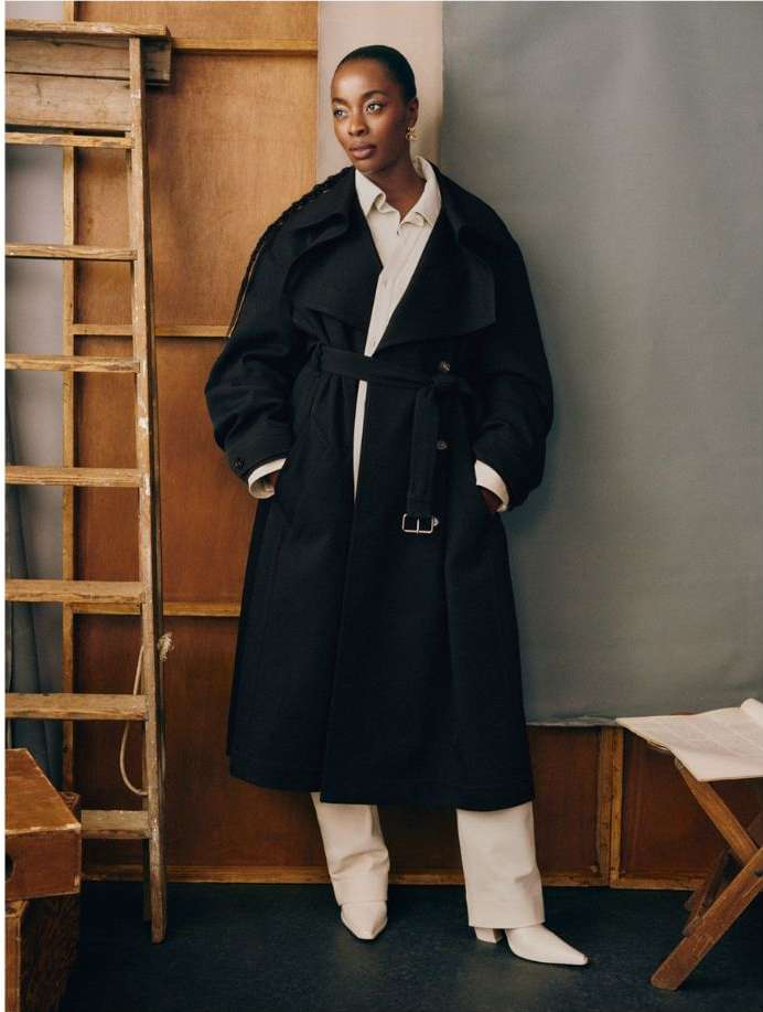 Elegant Black Woman in Trench Coat Posing in Studio. Full shot captures neutral colors, modern fashion, and timeless style.