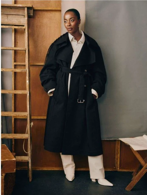 Elegant Black Woman in Trench Coat Posing in Studio. Full shot captures neutral colors, modern fashion, and timeless style.