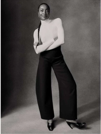 Black and white portrait of a woman wearing a turtleneck sweater and high-waisted trousers by Ben Weller.