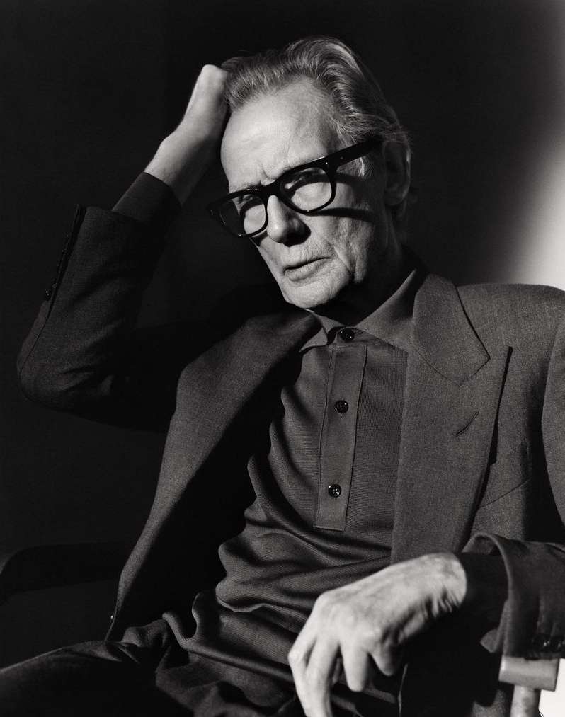 Black and white portrait of an elderly man wearing glasses and a suit, sitting in a chair with his hand on his head.