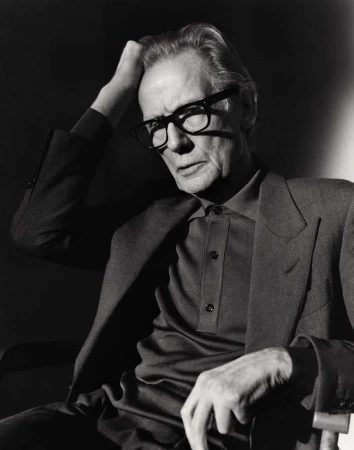 Black and white portrait of an elderly man wearing glasses and a suit, sitting in a chair with his hand on his head.