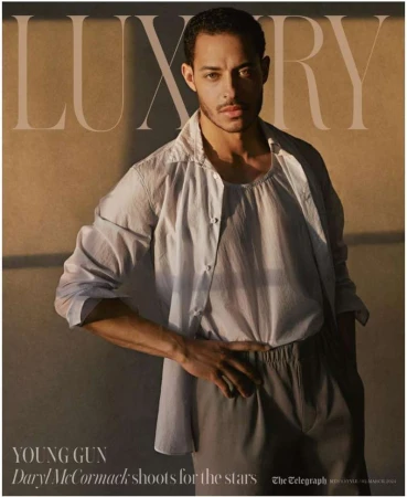 Portrait of actor Daryl McCormack on a magazine cover, wearing a white button-down shirt and gray pants, posing with a tan background.