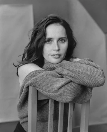 Monochrome portrait of a woman resting her crossed arms on the back of a wooden chair.