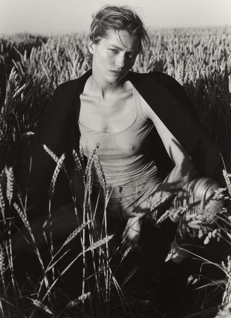 Monochrome portrait of a woman in a tank top and jacket in a wheat field, gazing intensely at the camera. Fashion, outdoor, beauty.