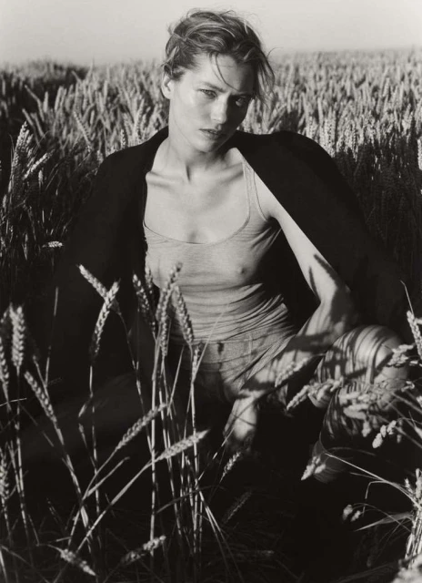 Monochrome portrait of a woman in a tank top and jacket in a wheat field, gazing intensely at the camera. Fashion, outdoor, beauty.
