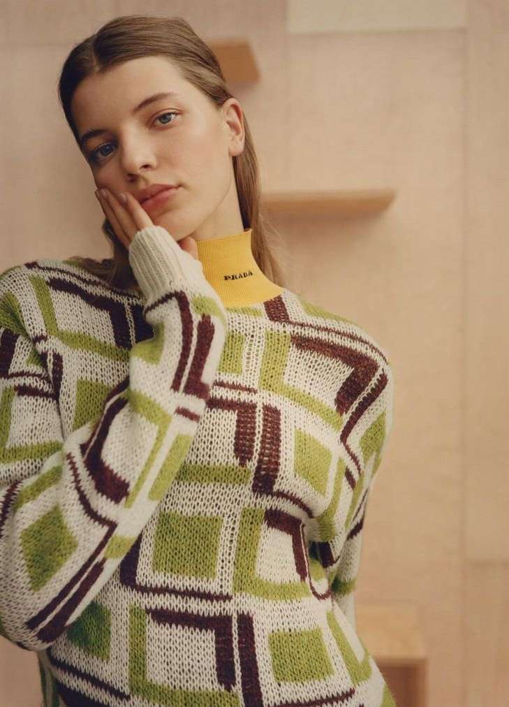 Model wearing a geometric patterned knit sweater with a yellow turtleneck collar posing indoors photographed by Ben Weller.