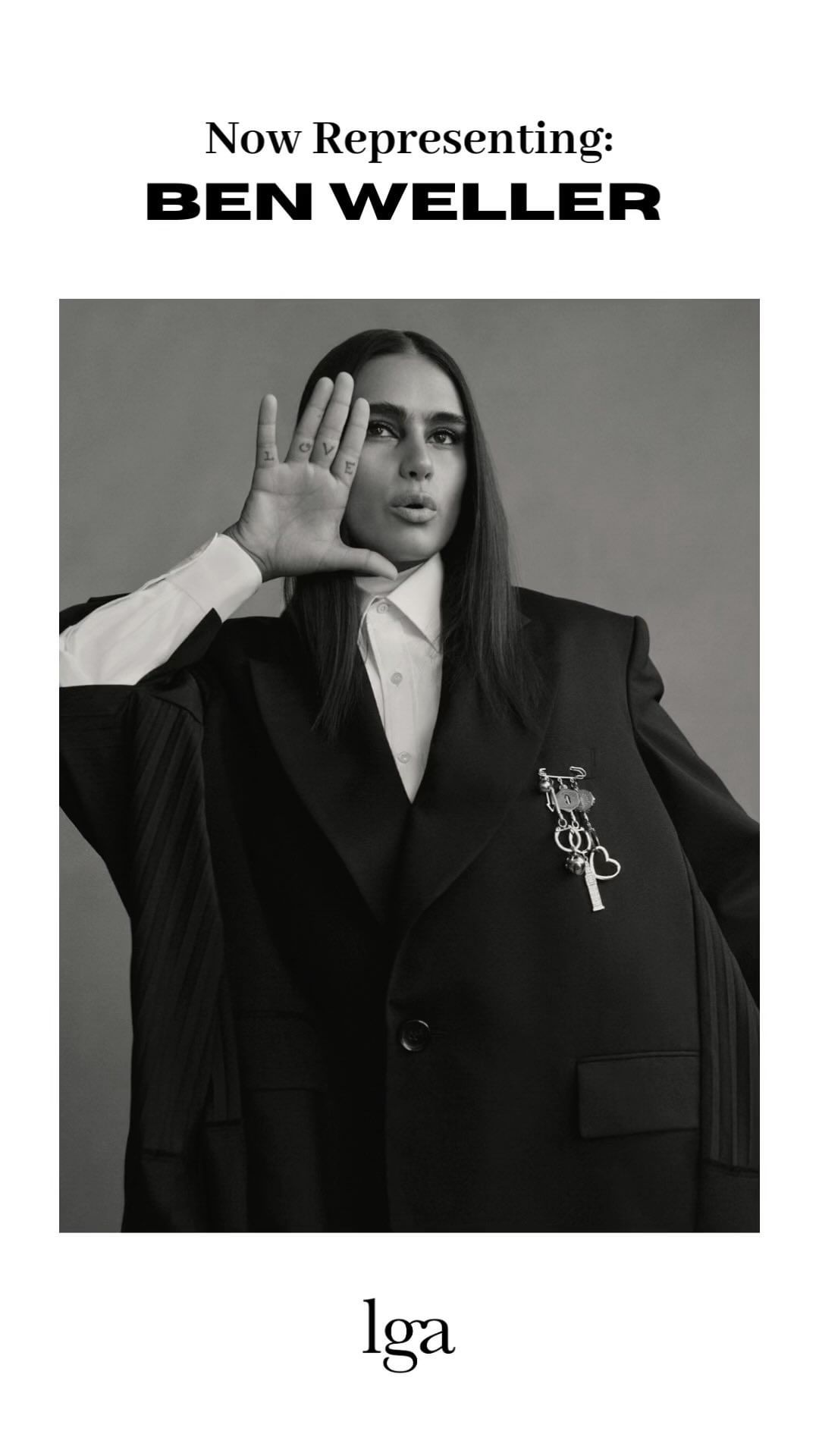 Portrait of a model wearing an oversized blazer and white shirt, set against a neutral grey backdrop in a black-and-white studio photograph.