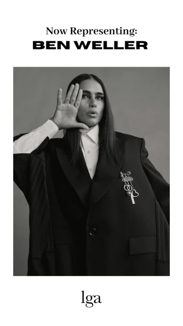 Portrait of a model wearing an oversized blazer and white shirt, set against a neutral grey backdrop in a black-and-white studio photograph.