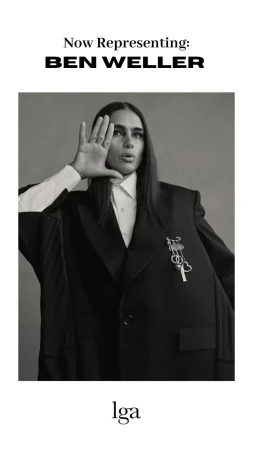 Portrait of a model wearing an oversized blazer and white shirt, set against a neutral grey backdrop in a black-and-white studio photograph.