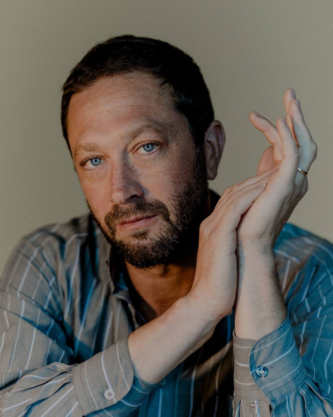 Portrait of a man with short brown hair and beard wearing a striped shirt against a plain wall