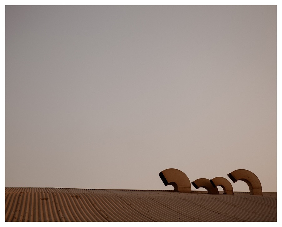 Minimalist photo of ventilation ducts on a ribbed roof against a soft gradient sky, emphasizing shape, texture, and architectural detail.