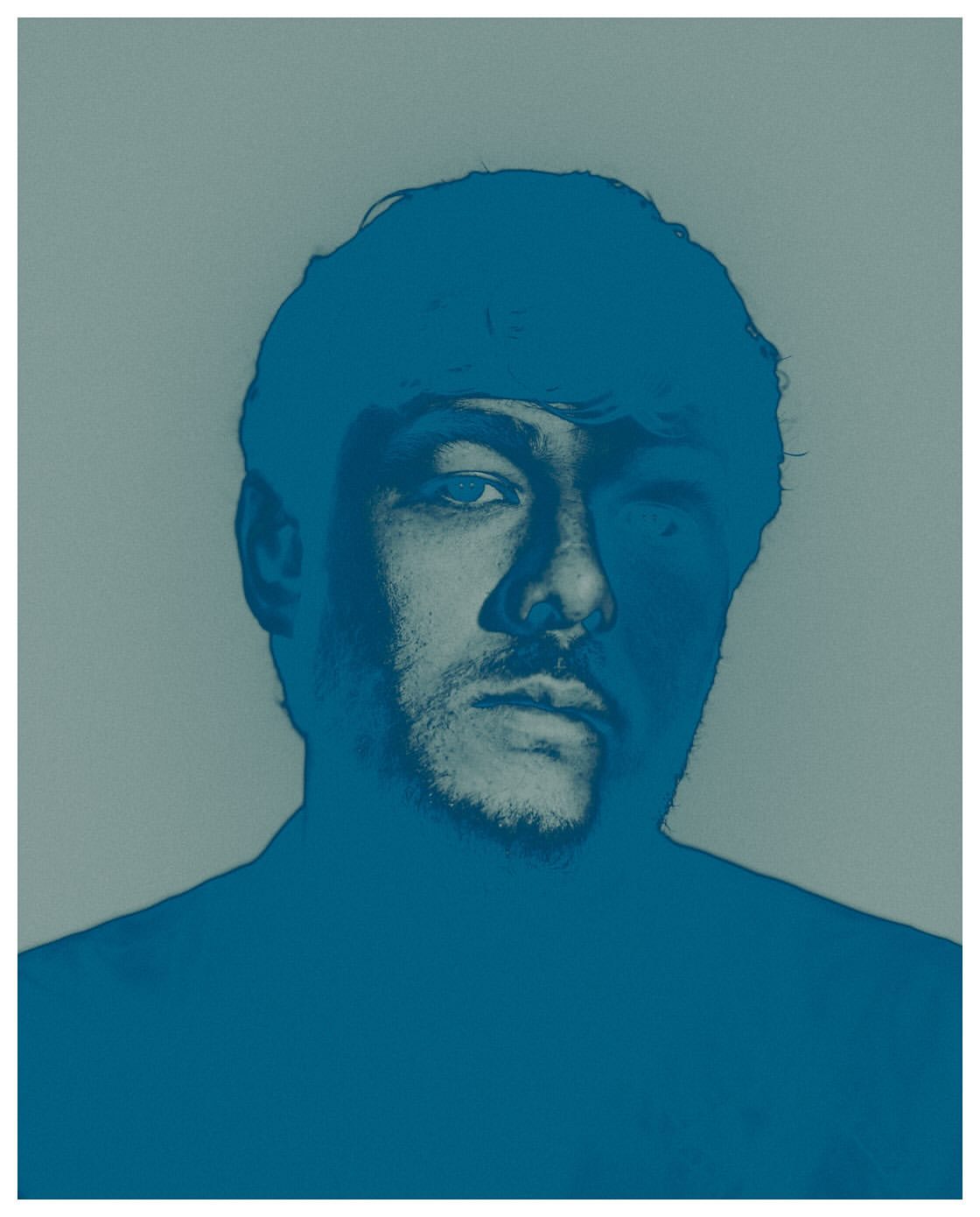 Monochromatic portrait of a man with short hair and stubble, rendered in shades of blue against a muted gray background.