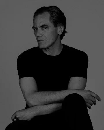 Portrait of a man wearing a black t-shirt with arms crossed against a plain grey background