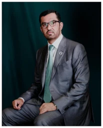 Man wearing a grey suit and green tie sitting against a dark textured backdrop in a portrait by Benedict Evans.